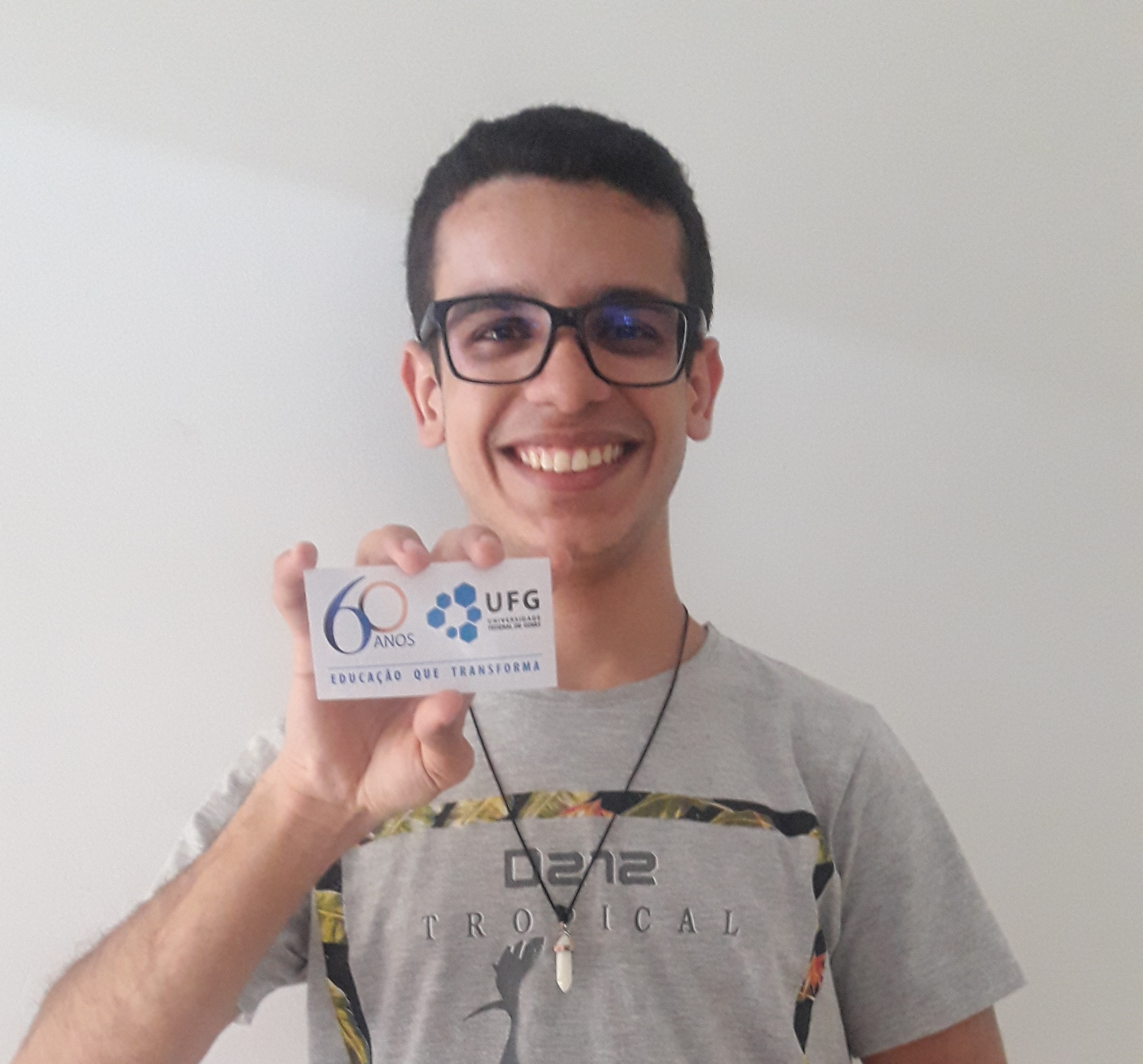 Foto de Gianlluca sorrindo e segurando um pequeno cartão de acolhimento da UFG
